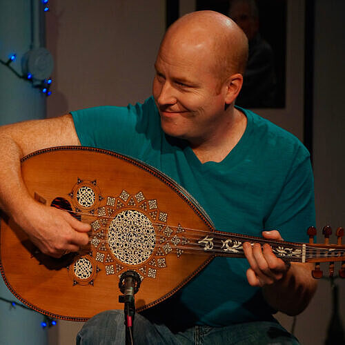 mac holding a oud wearing a turquoise shirt